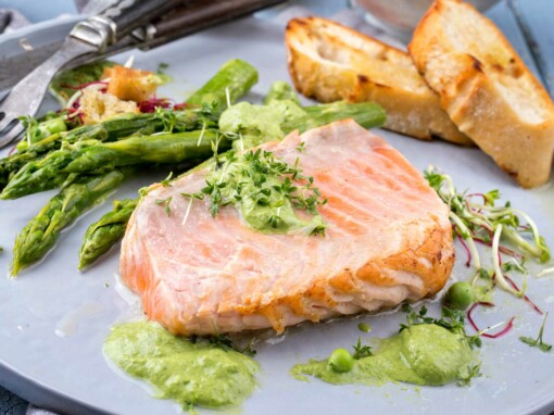 Pavé de saumon mi-cuit, asperges et sauce verte – Un généreux pavé de saumon mi-cuit, tendre et rosé à l’intérieur, servi avec une sauce verte onctueuse et parsemé de fines herbes fraîches. Accompagné d’asperges vertes croquantes et de tranches de pain grillé, ce plat allie fraîcheur et gourmandise pour une dégustation saine et savoureuse.